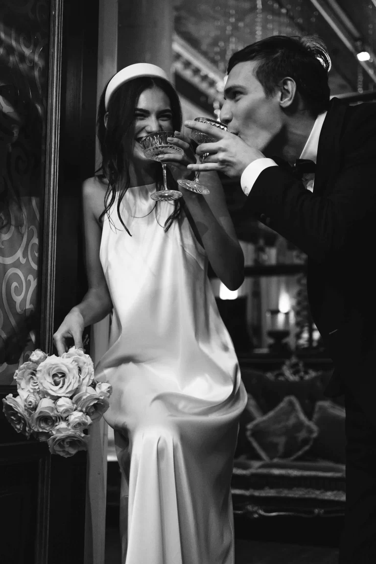 wedding couple drinking,Elegant wedding dress with intricate lace details hanging in a rustic stone room with a wooden beam ceiling and soft natural lighting